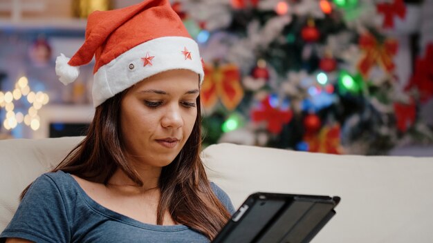 Foto close-up de uma mulher com chapéu de papai noel segurando um tablet digital