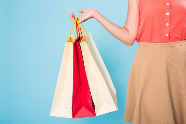 Close-up de uma mulher com sacolas de compras coloridas na parede azul