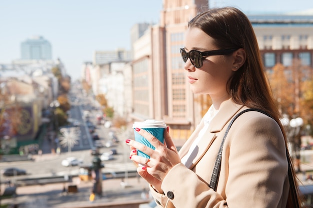 Close-up de uma mulher de óculos escuros, tomando café na cidade