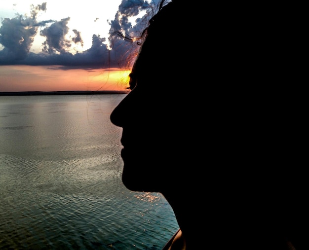 Foto close-up de uma mulher em silhueta de pé na praia durante o pôr do sol