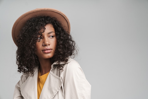 Close-up de uma mulher jovem e atraente africana com cabelo encaracolado, vestindo um casaco de outono e um chapéu