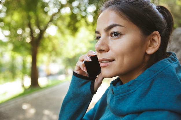 Close-up de uma mulher jovem e atraente fitness vestindo roupas esportivas, fazendo exercícios ao ar livre, usando telefone celular