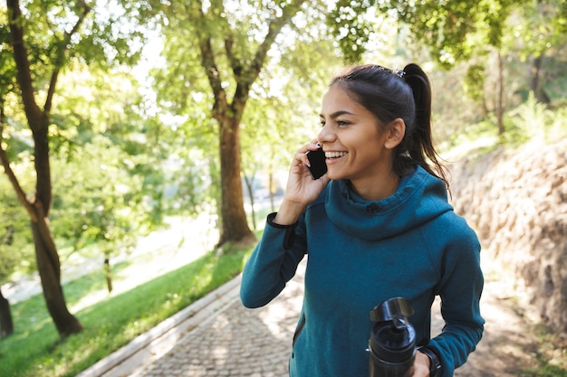 Close-up de uma mulher jovem e atraente fitness vestindo roupas esportivas, fazendo exercícios ao ar livre, usando telefone celular