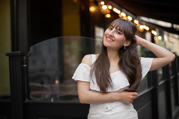 Close-up de uma mulher morena sorridente com cabelos longos, em um vestido branco no fundo de um café e lanternas amarelas. lugar para o seu design