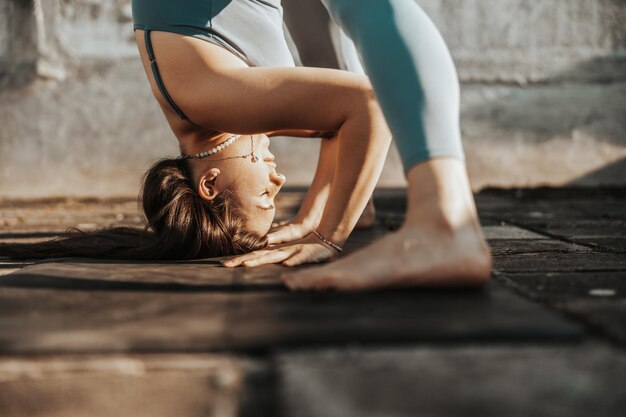 Foto close-up de uma mulher praticando exercícios de alongamento de ioga em um terraço ao pôr do sol.