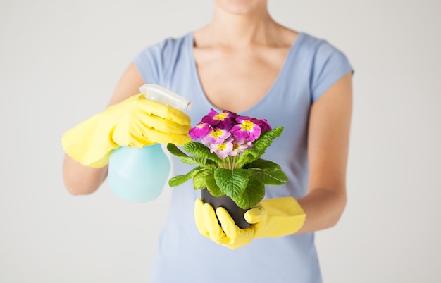 close-up de uma mulher segurando o pote com uma flor e um frasco de spray