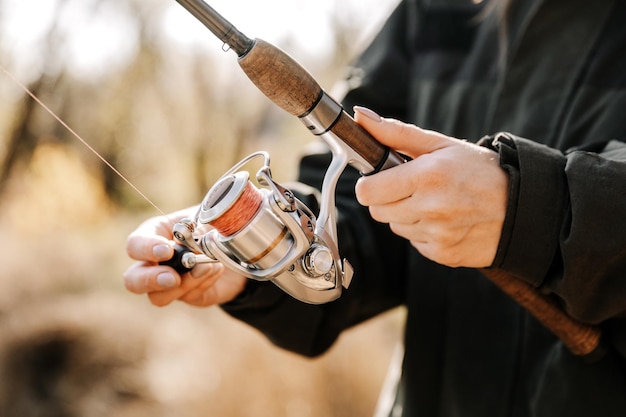 Close-up de uma mulher segurando uma vara de pescar com um carretel, pesca esportiva.