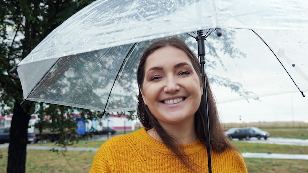 Close-up de uma mulher sob um guarda-chuva transparente em tempo chuvoso.