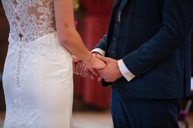 Close-up de uma noiva e um noivo de mãos dadas durante a cerimônia de casamento