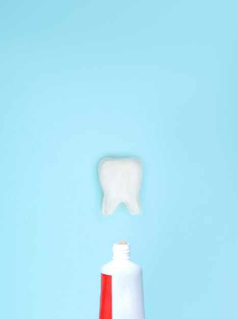 Foto close-up de uma pasta de dentes e modelo de dente em fundo azul desfocado significa cuidar da cavidade oral