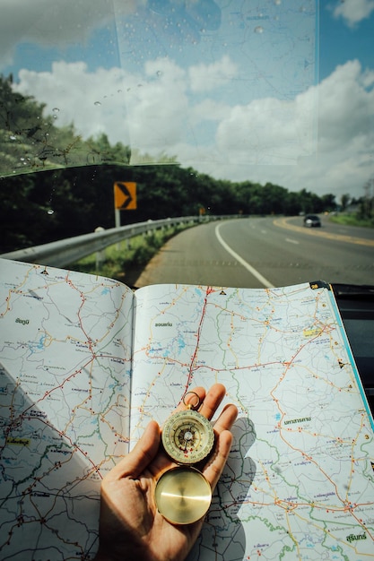 Foto close-up de uma pessoa com a mão segurando uma bússola de navegação com um mapa no pára-brisas de um carro