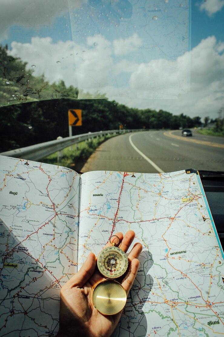 Foto close-up de uma pessoa com a mão segurando uma bússola de navegação com um mapa no pára-brisas de um carro