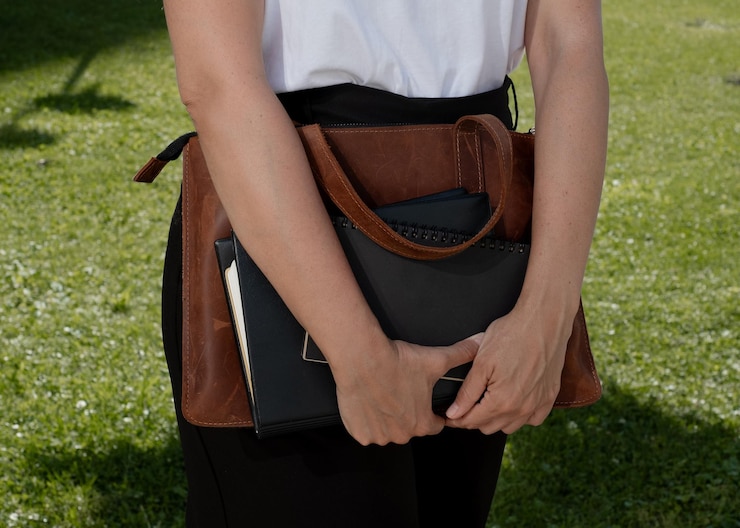 Foto close-up de uma pessoa segurando uma bolsa de laptop e um caderno ao ar livre