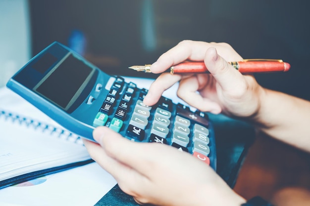 Close-up de uma pessoa segurando uma caneta enquanto usa uma calculadora na mesa