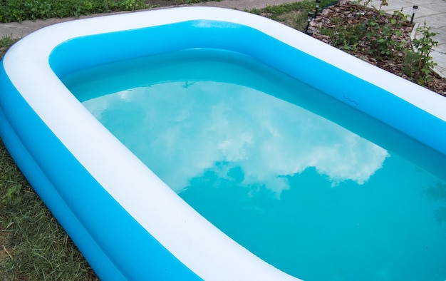 Close-up de uma piscina inflável de pé na grama em um dia de verão ensolarado o reflexo de nuvens na superfície da água