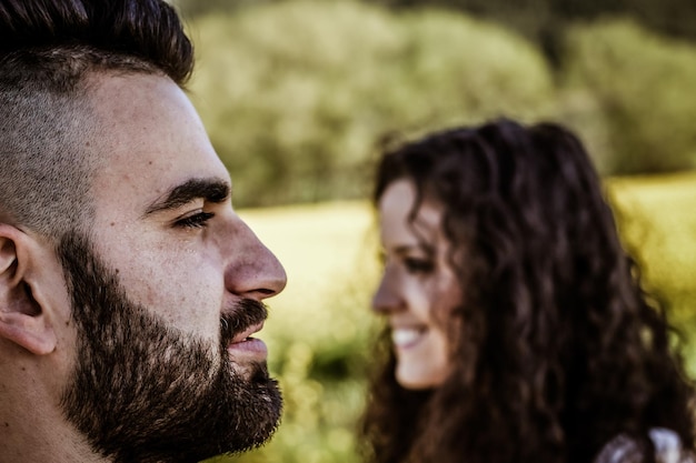 Close-up de uma vista de perfil de um rosto sorridente de homem barbudo em primeiro plano e um rosto sorridente de mulher em perfil ao fundo fundo horizontal amarelo natural