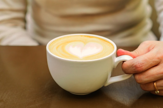 Close-up de uma xícara grande de cappuccino acabado de fazer com espuma macia e açúcar mascavo e coração de desenho por barista