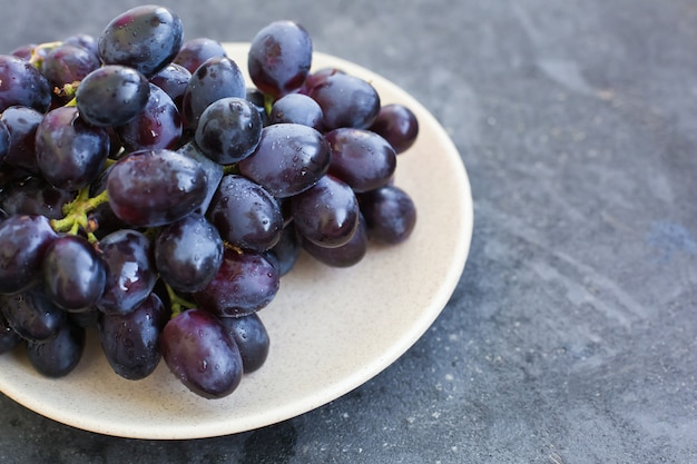 Close-up de uvas azuis maduras em um prato em um fundo gasto concreto azul