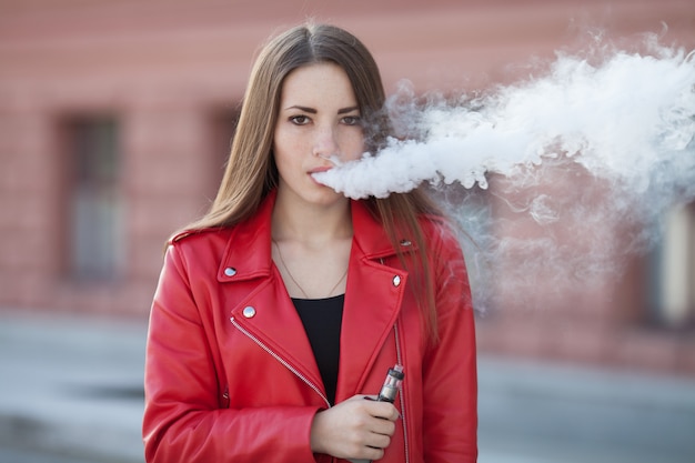 Close-up de vaping jovem garota segurando o dispositivo e-cig moderno nos lábios. Nicotina de fumar de qualidade. Mulher jovem fumante com dispositivo de cigarro eletrônico.