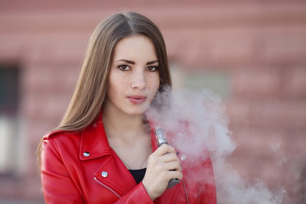 Close-up de vaping jovem garota segurando o dispositivo e-cig moderno nos lábios. Nicotina de fumar de qualidade. Mulher jovem fumante com dispositivo de cigarro eletrônico.