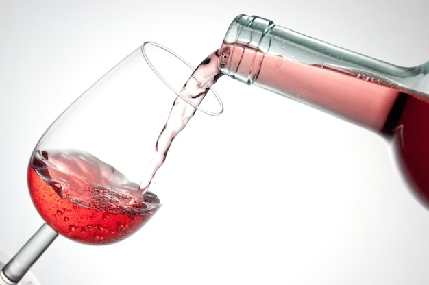 Close-up de vinho a ser derramado de garrafa em copo contra fundo branco