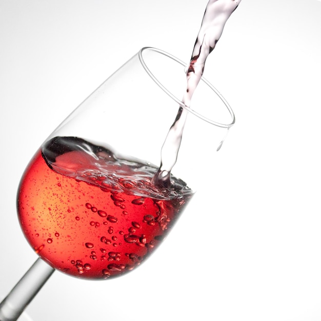 Close-up de vinho vermelho derramando em copo contra fundo branco.