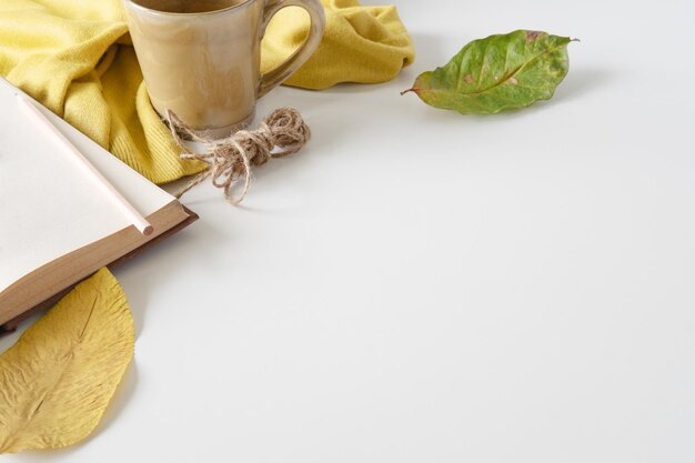 Foto close-up de xícara de café por livro e lápis com folhas secas na mesa sobre fundo branco