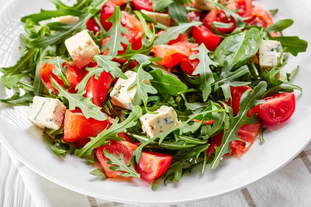 Close-up de deliciosa ensalada de tomate, queso azul y rúcula de salmón saludable en una placa blanca.