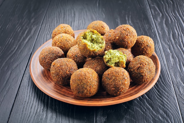 Close-up de deliciosas bolas de falafel y uno se rompe en pedazos en una placa de arcilla sobre la mesa de madera negra