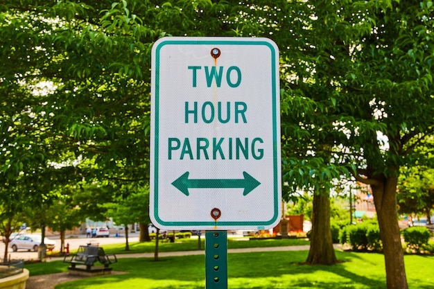 Close-up des grünen Zwei-Stunden-Parking-Zeichens vor einem Park im Sommer