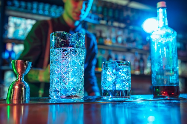 Close up do barman termina a preparação de um coquetel alcoólico em luz neon multicolorida