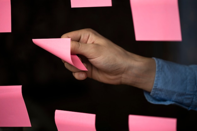 Close-up do braço masculino arrancando o bilhete de papel rosa adesivo do quadro