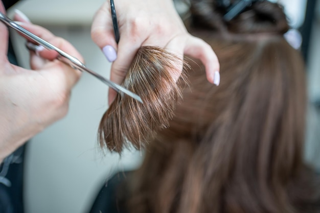 Close-up do cabeleireiro feminino faz penteado na mulher morena no salão de corte de cabelo com tesoura