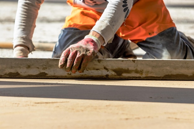 Close-up do construtor de homem colocando trilho de mesa no chão coberto com mistura de areia no canteiro de obras Trabalhador masculino nivelando a superfície com borda reta enquanto nivela o piso Fundo desfocado