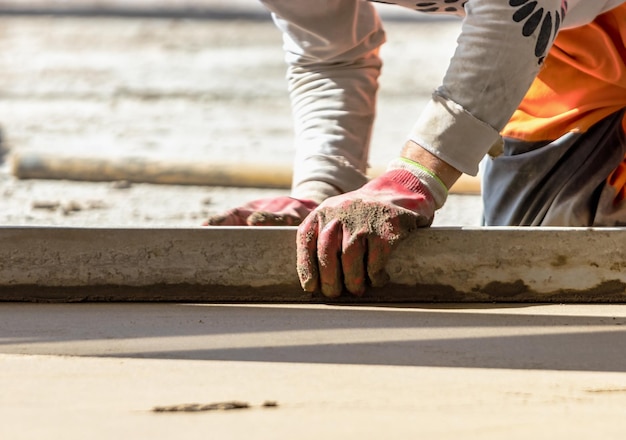 Close-up do construtor de homem colocando trilho de mesa no chão coberto com mistura de areia no canteiro de obras Trabalhador masculino nivelando a superfície com borda reta enquanto nivela o piso Fundo desfocado