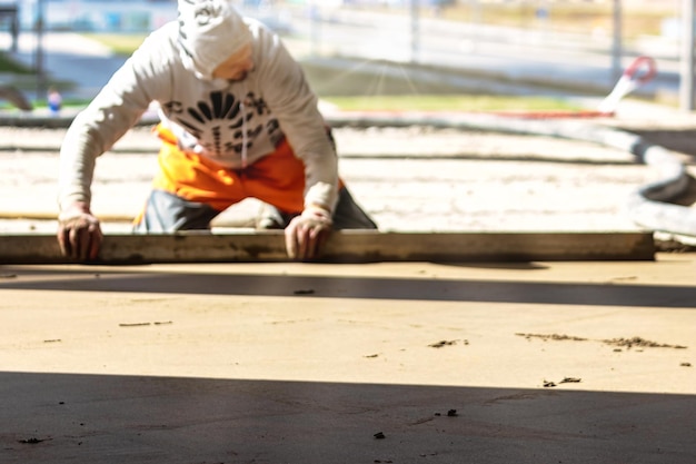 Close-up do construtor de homem colocando trilho de mesa no chão coberto com mistura de areia no canteiro de obras Trabalhador masculino nivelando a superfície com borda reta enquanto nivela o piso Fundo desfocado
