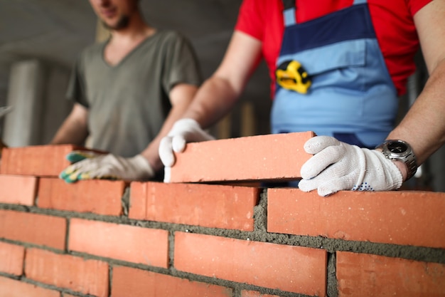 Close-up do construtor que coloca o tijolo com o profissional. Trabalhadores no trabalho, pedreiros construindo paredes, empreiteiro e trabalhador.