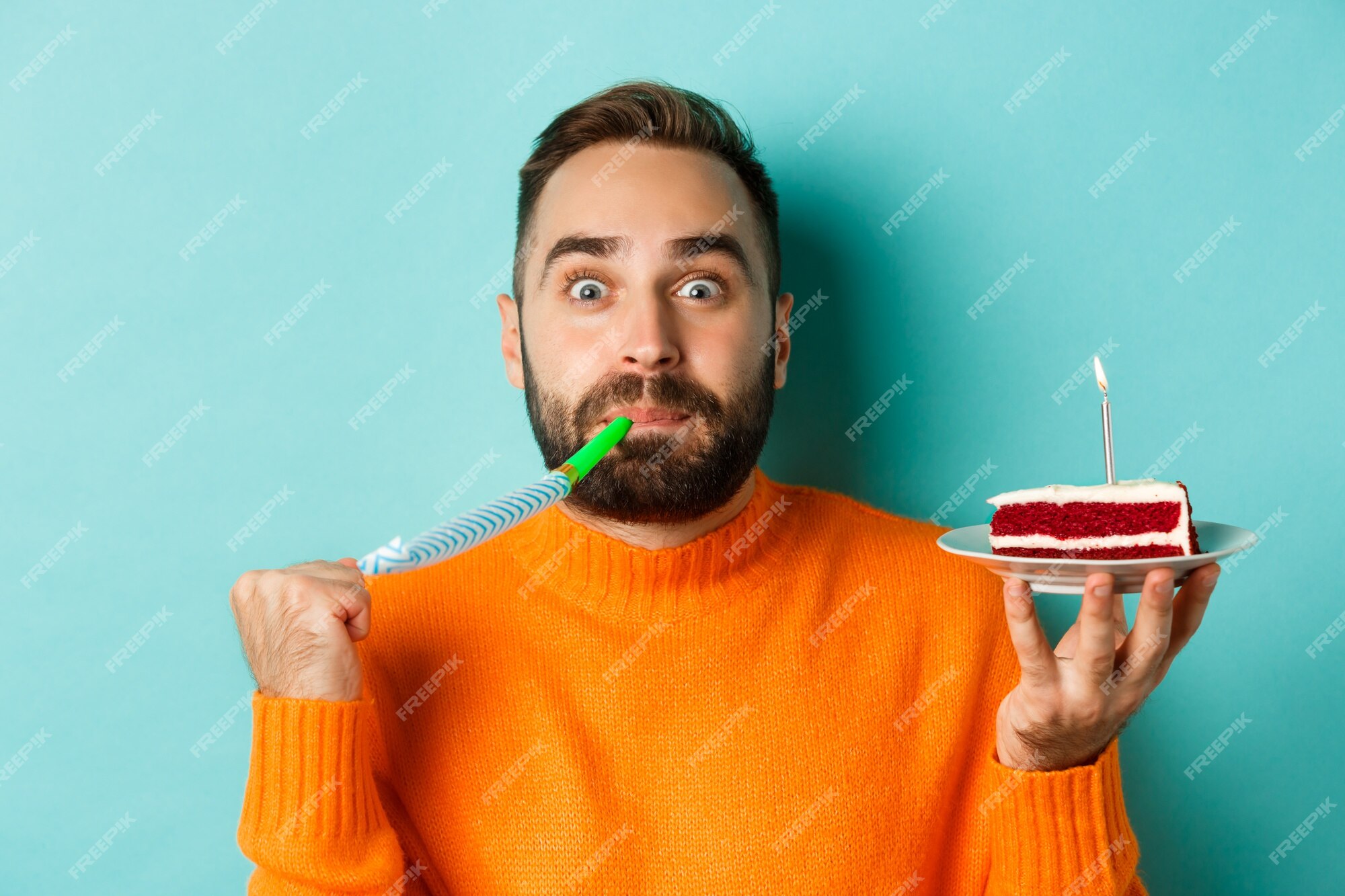 Close-up do homem adulto engraçado comemorando seu aniversário, segurando o  bolo bday com vela, soprando wistle festa e regozijando-se, em pé sobre  fundo azul claro.