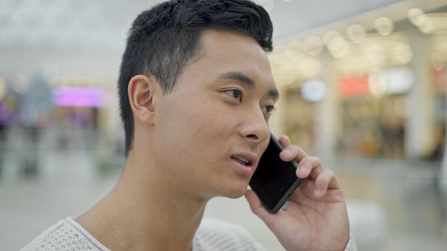 Close-up do homem asiático falando ao telefone no fundo do shopping