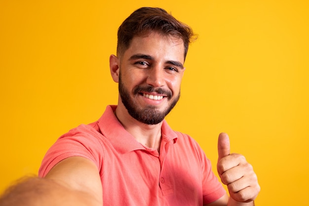 Close-up do homem bonito, fazendo selfie com o polegar para cima fazendo polegares para cima ok.