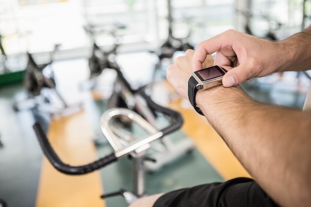 Close up do homem usando smartwatch na bicicleta de exercício no ginásio