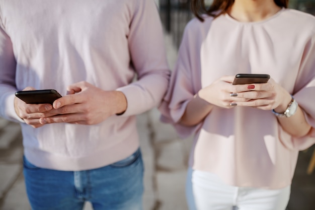 Close-up do jovem casal usando telefones inteligentes ao ar livre