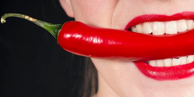 Foto close-up do meio de uma mulher com pimenta vermelha sobre fundo preto