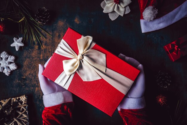 Close up do Papai Noel com mãos usando luvas brancas e segurando um presente de Natal