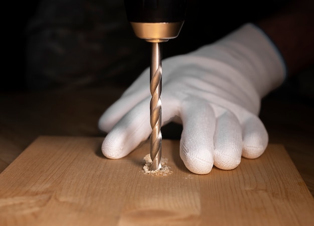 Close up do processo de trabalho de perfuração. Broca de aço moderna que faz furos em madeira e mãos em luvas de construtor.