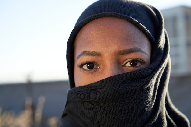 Close-up do rosto de uma jovem muçulmana com hijab, olhando para a câmera.