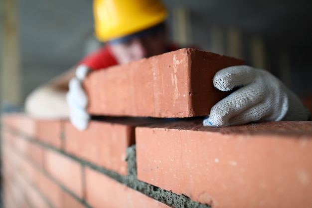 Foto close-up do trabalhador da construção profissional que coloca tijolos no local industrial. construtor em uniforme de proteção. parede de edifício de homem com blocos. conceito de renovação