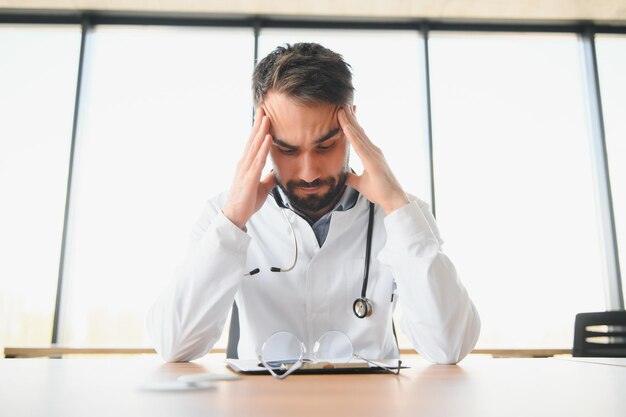 Close-up do trabalhador médico cansado chateado fechando a cabeça com as mãos Médico deprimido sentado no escritório estetoscópio no pescoço de pessoas Medicina moderna e conceito de saúde