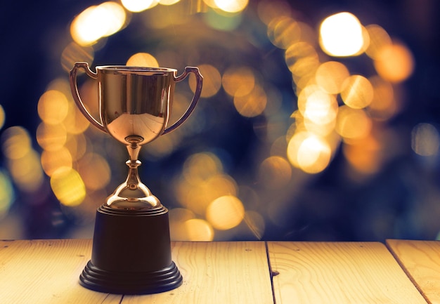 Close-up do troféu dourado em uma mesa de madeira contra um fundo desfocado