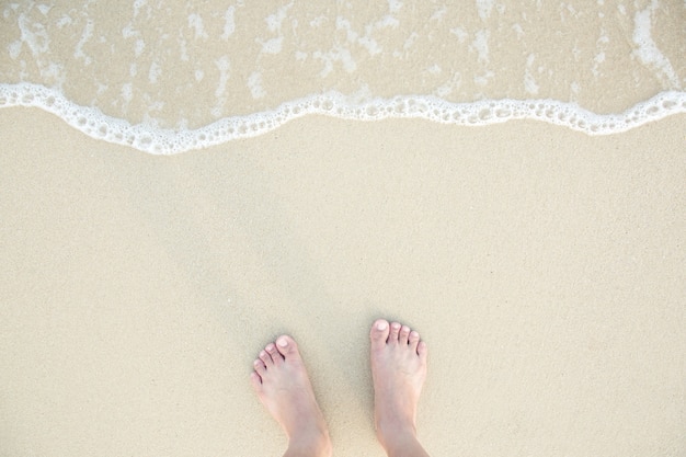 Close Up dos pés descalços de um homem molhado na praia, com uma borda de areia suavemente abaixo deles. Férias na praia do oceano, pé na areia do mar.